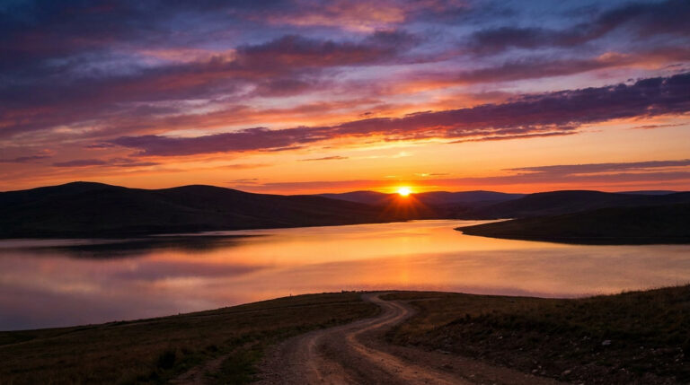 Coucher du soleil aujourd’hui : l’heure et les infos clés Soleil couchant éclatant sur un vaste lac, entouré de collines sombres, avec des nuages oranges et violets.