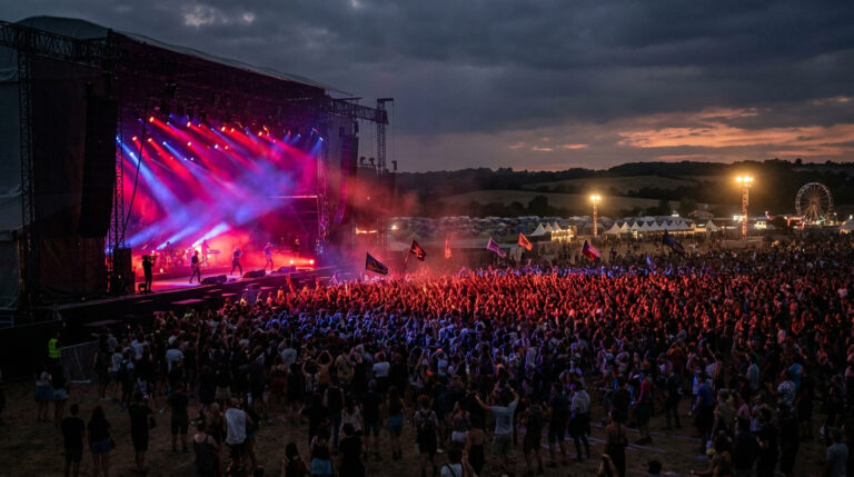 Hellfest 2025 : ton guide pour survivre à Clisson Une immense foule devant une scène de concert illuminée de rouge et bleu lors d'un festival de métal au crépuscule.