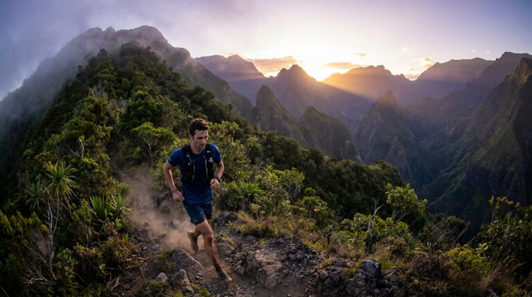 Un coureur de trail court sur un sentier montagneux escarpé à La Réunion, sous un lever de soleil spectaculaire.
